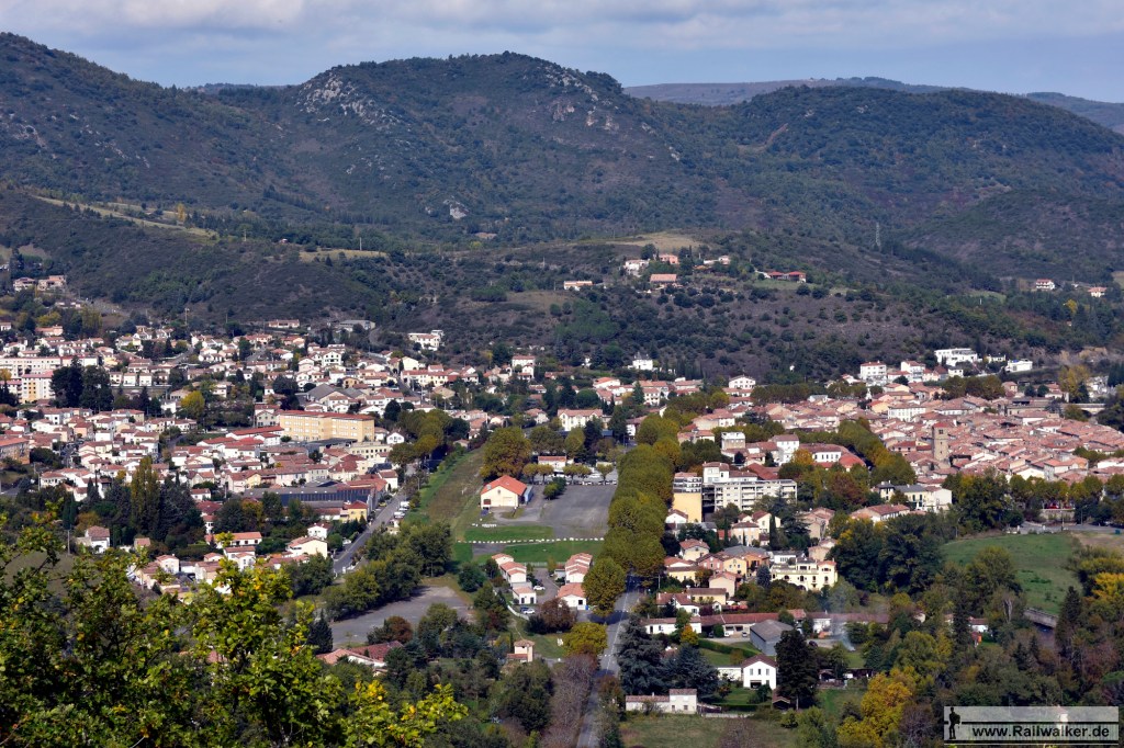 Aussicht auf Quillan. In der Bildmitte befindet sich das Bahnhofsareal. Das Bahnhofsgebäude selbst ist hinter den Bäumen verdeckt. Davor steht der Güterschuppen.